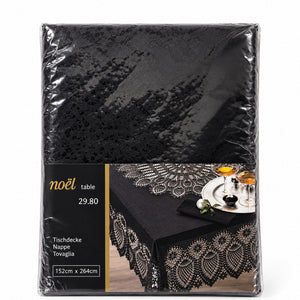 A black tablecloth with an intricate lace-like floral border, shown in its clear plastic retail packaging with a printed label. The label features the brand name 'noël' and displays a lifestyle image of the tablecloth styled on a table with glasses and a napkin.