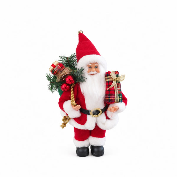 A festive Christmas Santa Claus figurine wearing a red suit with white fur trim, carrying a green pine bundle with red ornaments and a gift sack on one shoulder and a wrapped present on the other, set against a plain white background.