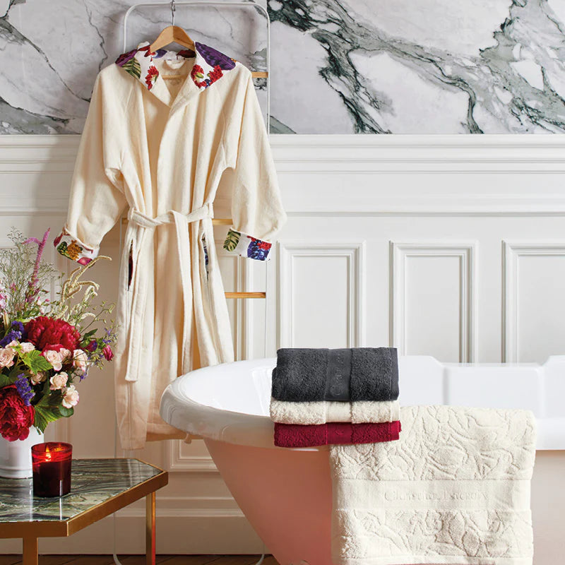 Beige robe with floral embroidery on a hanger, towels on a bathtub, and a candle on a table in a bathroom setting.