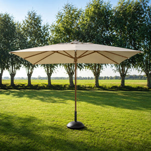 A large patio umbrella with a beige canopy and a dark base stands on a green lawn in front of a row of trees under a blue sky.