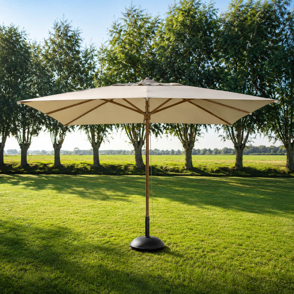 A large patio umbrella with a beige canopy and a dark base stands on a green lawn in front of a row of trees under a blue sky.
