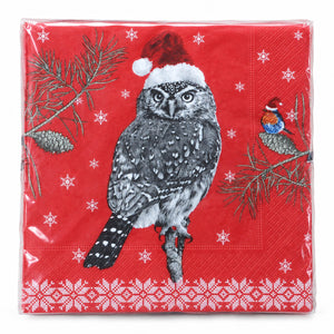 A square red paper napkin wrapped in clear plastic, printed with a black-and-white owl wearing a Santa hat, pine branches, snowflakes, and a small bird on a branch.