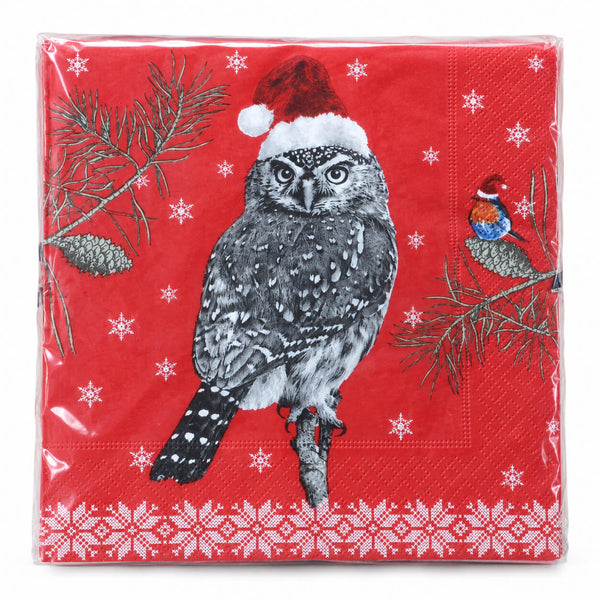 A square red paper napkin wrapped in clear plastic, printed with a black-and-white owl wearing a Santa hat, pine branches, snowflakes, and a small bird on a branch.