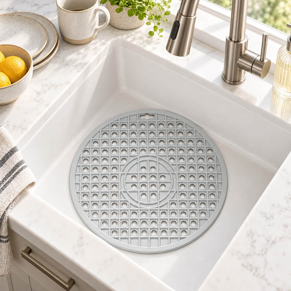 A round gray silicone kitchen mat with a textured grid pattern, placed inside a white farmhouse-style kitchen sink.