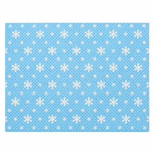 A rectangular blue fabric item, likely a placemat or mat, featuring a repeating pattern of white snowflakes and small white dots on a light blue background.