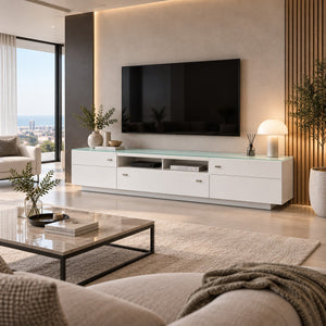A modern white TV console with a translucent green-tinted glass top, styled in a contemporary living room with a wall-mounted television, a glass coffee table, and a beige sofa.