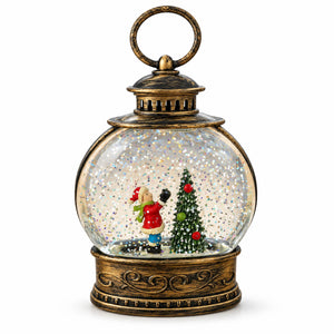 A decorative lantern-shaped snow globe with an antique bronze metal frame, featuring a small Christmas tree and two miniature figures inside, set against a plain white background.