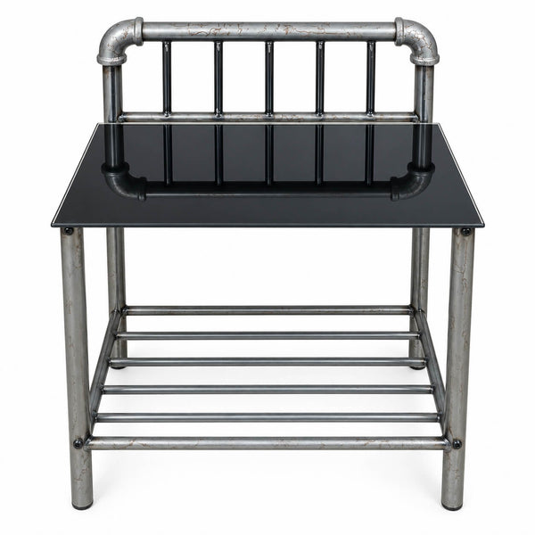 Industrial-style end table featuring a black glass top and a weathered silver metal frame with pipe details on the backrest and lower shelf, shown against a plain white background.