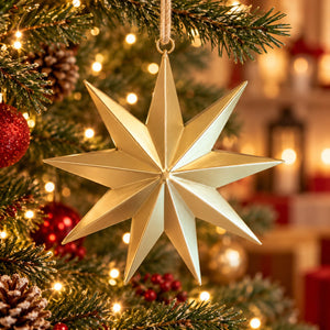 A metallic gold 12-point star Christmas ornament hanging from a tree branch with warm holiday lights and blurred ornaments in the background.