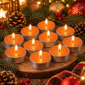 Eight lit orange glitter tea light candles arranged on a round wooden tray, surrounded by pine branches, pinecones, red berries, and holiday ornaments in a warm festive setting.