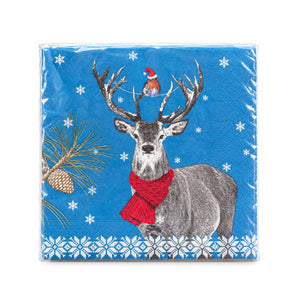 A square paper napkin wrapped in clear plastic, featuring a blue winter holiday design with a gray deer wearing a red knit scarf, a small bird in a Santa hat, pine branches, snowflakes, and a white snowflake border.