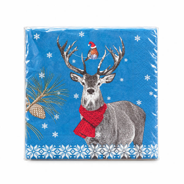 A square paper napkin wrapped in clear plastic, featuring a blue winter holiday design with a gray deer wearing a red knit scarf, a small bird in a Santa hat, pine branches, snowflakes, and a white snowflake border.