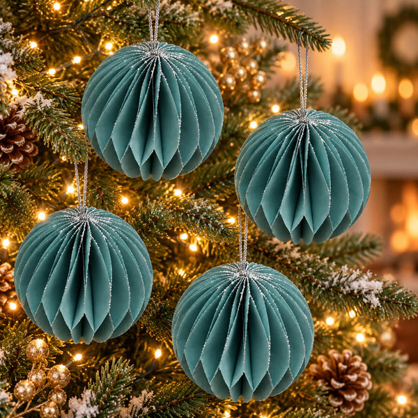 Four teal paper honeycomb Christmas ornaments hanging on a decorated Christmas tree with warm lights and pinecones.