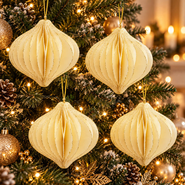 Four cream-colored, honeycomb-style paper Christmas ornaments hanging on a decorated Christmas tree with warm string lights, pinecones, and gold ornaments.