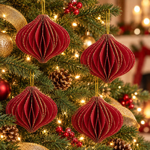 Three red honeycomb paper Christmas ornaments with gold glitter trim hanging on a decorated Christmas tree with warm lights, pinecones, and gold ornaments.