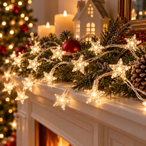 Warm white star-shaped Christmas string lights draped over a white fireplace mantel with green garland, candles, ornaments, and a small house decoration in a cozy holiday setting.