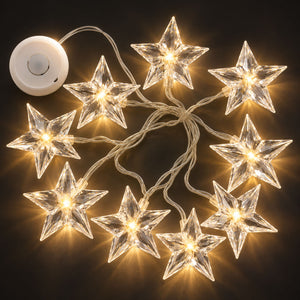 Twelve clear crystal star-shaped string lights glowing with warm yellow light, connected by a white wire with a white power button controller, set against a solid black background.
