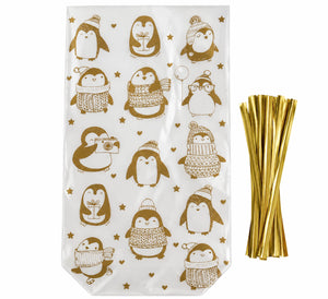White gift bags printed with brown penguin illustrations wearing winter hats and scarves, shown next to a bundle of metallic gold straws on a white background.