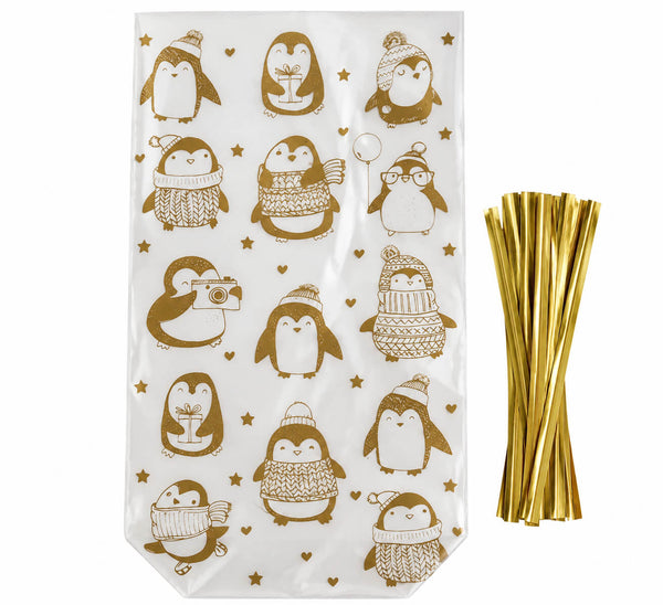 White gift bags printed with brown penguin illustrations wearing winter hats and scarves, shown next to a bundle of metallic gold straws on a white background.