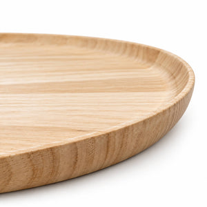 A close-up of a round wooden serving tray with a natural light oak finish, showing the wood grain texture and curved rim, set against a clean white background.