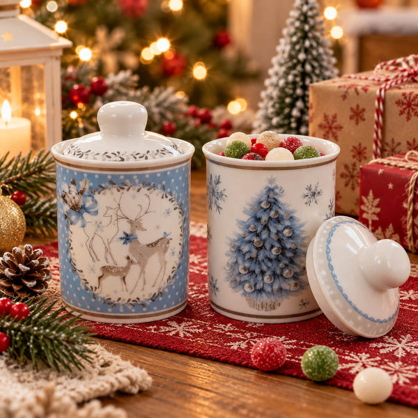 Two decorative ceramic Christmas canisters on a red patterned runner, surrounded by holiday decorations including pine branches, ornaments, wrapped gifts, and a blurred Christmas tree in the background.