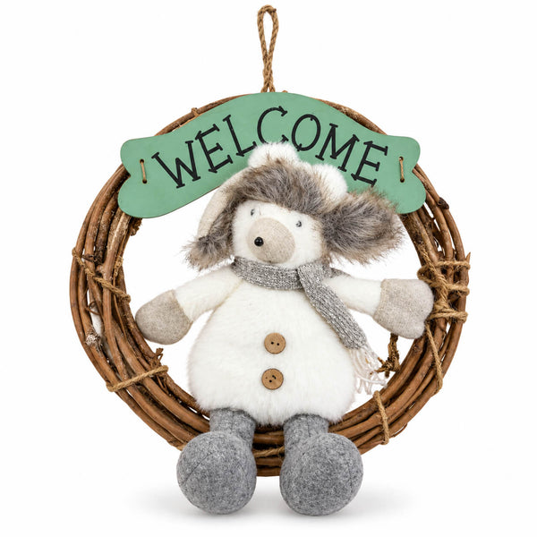 A plush winter snowman hanging from a woven wicker wreath with a green 'WELCOME' sign. The snowman has white fur, gray felted legs and scarf, and brown buttons.