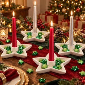 Three white ceramic star-shaped candle holders with lit taper candles are arranged on a decorated Christmas table runner. The holders contain shiny green star-shaped ornaments, with a blurred festive background showing a Christmas tree, gifts, and warm string lights.