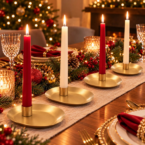 Four gold candlesticks with red and white taper candles arranged on a decorated Christmas table runner, with warm holiday lights and a blurred festive background.