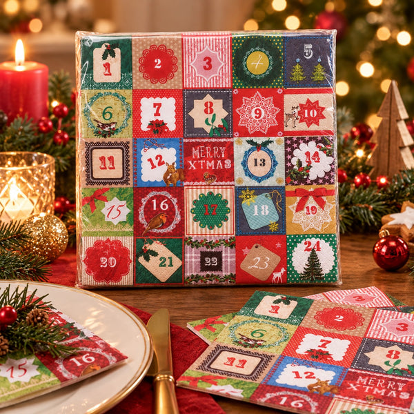 A Christmas advent calendar made of colorful patchwork fabric squares, shown on a decorated wooden table with candles, pine branches, ornaments, and a plate. Several numbered fabric pockets are pulled out in front.