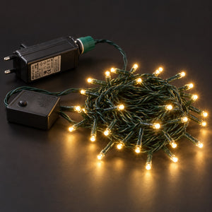 Warm white Christmas string lights with a green wire, shown coiled with two black power adapters on a dark background.