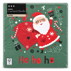 A pack of square paper napkins from Migros Cucina & Tavola, featuring a festive Christmas design with Santa Claus, a large red sack, candy canes, and 'Ho ho ho' printed on a dark green background.
