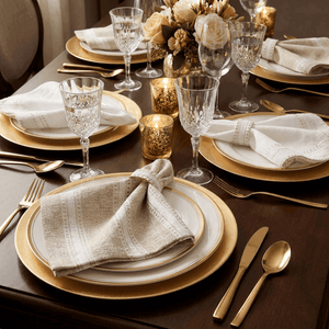 Elegant table setting with gold and white plates, glasses, and silverware on a dark surface.