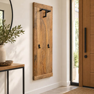 A rustic vertical wooden wall hook rack with black metal hardware, mounted on a white wall in a modern entryway next to a wooden door and console table.
