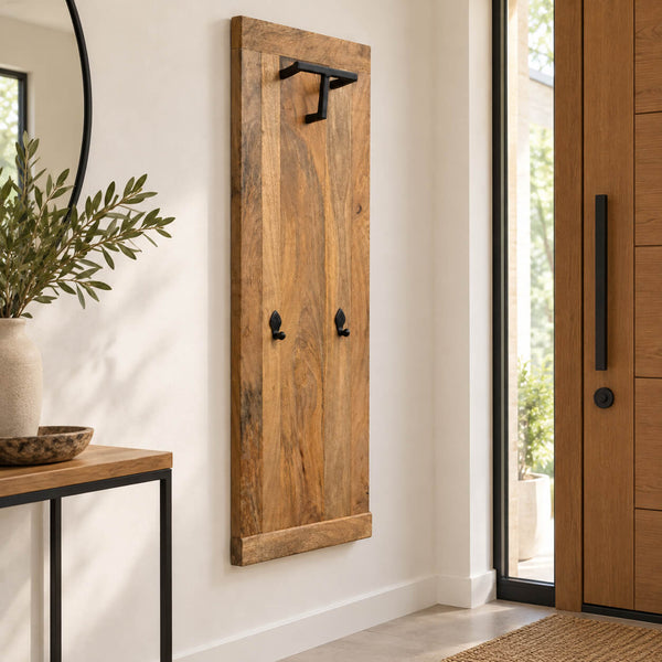 A rustic vertical wooden wall hook rack with black metal hardware, mounted on a white wall in a modern entryway next to a wooden door and console table.