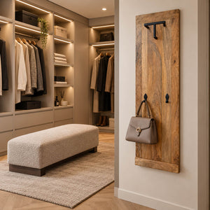 A rustic wooden entryway coat rack with black metal hooks hangs on a wall in a modern walk-in closet. A taupe handbag is hanging from one of the hooks, with clothing and shelving visible in the background.