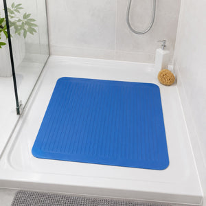 A blue rectangular shower mat with a ribbed non-slip texture placed on a white bathtub in a tiled bathroom setting.