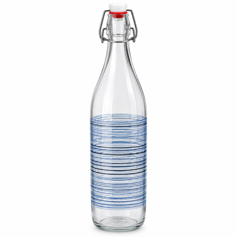 Two tall clear glass swing-top bottles filled with olive oil, standing on a kitchen counter with bread, basil, olives, and kitchen items in the background.