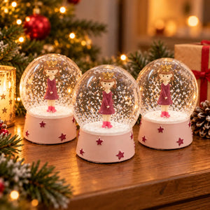 Three Migros Christmas girl snow globes displayed together in festive décor
