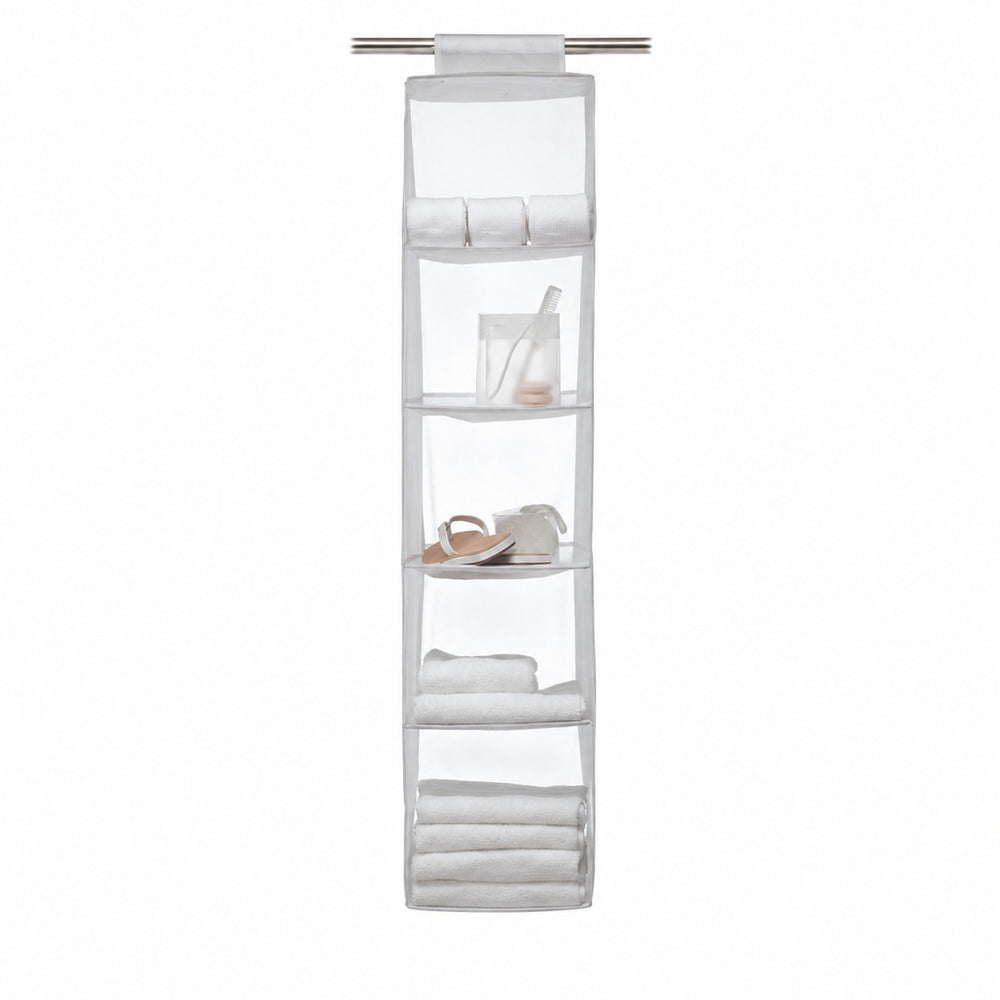 A white fabric closet organizer hanging from a metal rod inside a white closet, holding folded towels, rolled towels, a small jar, and a pair of sandals. Clothes are visible on hangers to the left.