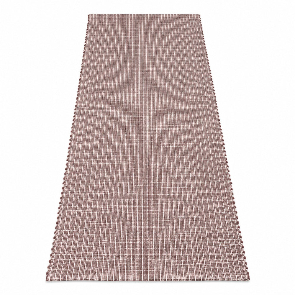 A rectangular woven table runner in a muted mauve-brown color with thin vertical white stripes, styled on a wooden dining table with plates, wine glasses, and a small vase of greenery.