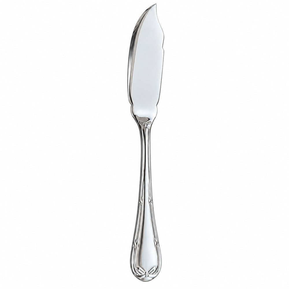 A silver butter knife with an ornate handle rests on a beige tablecloth beside a plated meal of grilled fish, asparagus, potato, and lemon. A folded cream napkin and part of a white plate are visible in the foreground, with a wine glass and flowers in the background.