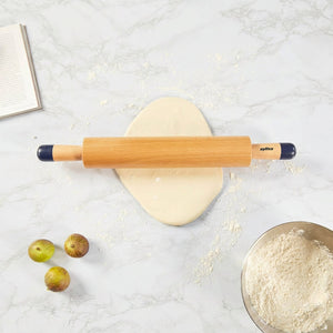 Wooden rolling pin on a marble surface with a bowl of flour and apples.