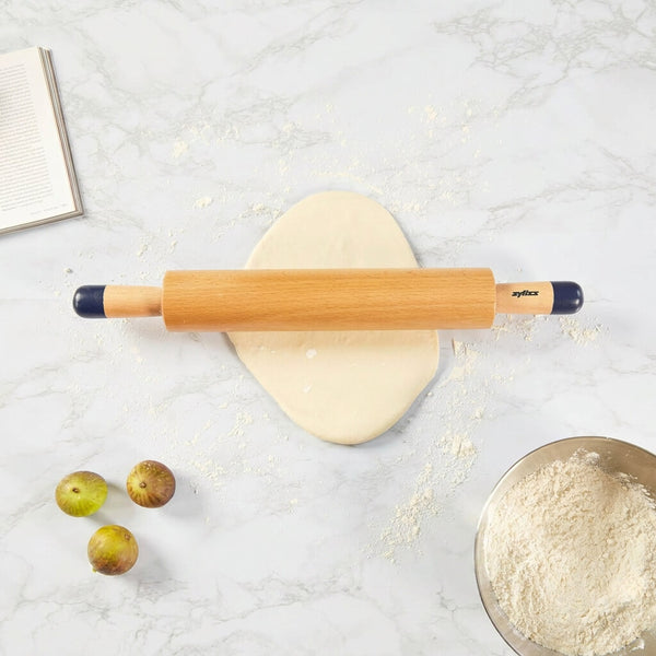 Wooden rolling pin on a marble surface with a bowl of flour and apples.