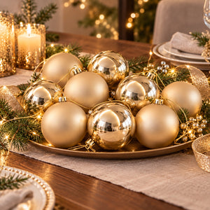 A set of metallic gold Christmas baubles arranged on a bronze tray with pine branches and warm string lights on a dining table.