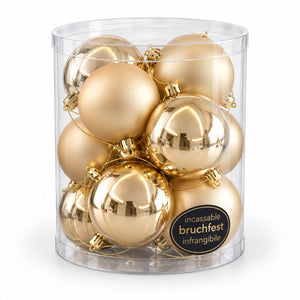 A clear cylindrical container filled with shiny metallic gold Christmas ornaments, with a black circular label reading 'incassable bruchfest infrangible' on the front, photographed on a white background.