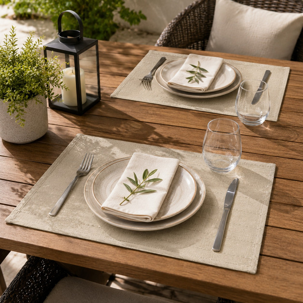 ALT Text
Set of 2 beige woven placemats styled on a wooden outdoor dining table with neutral dinnerware, cutlery, glasses, and decorative greenery in a sunny patio setting.