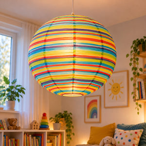 A colorful striped spherical pendant lamp glowing with warm light, hanging in a cozy child's room with shelves, plants, and framed wall art.