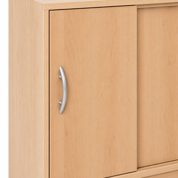 Close-up of a light natural wood cabinet with a curved silver metal handle on a white background.