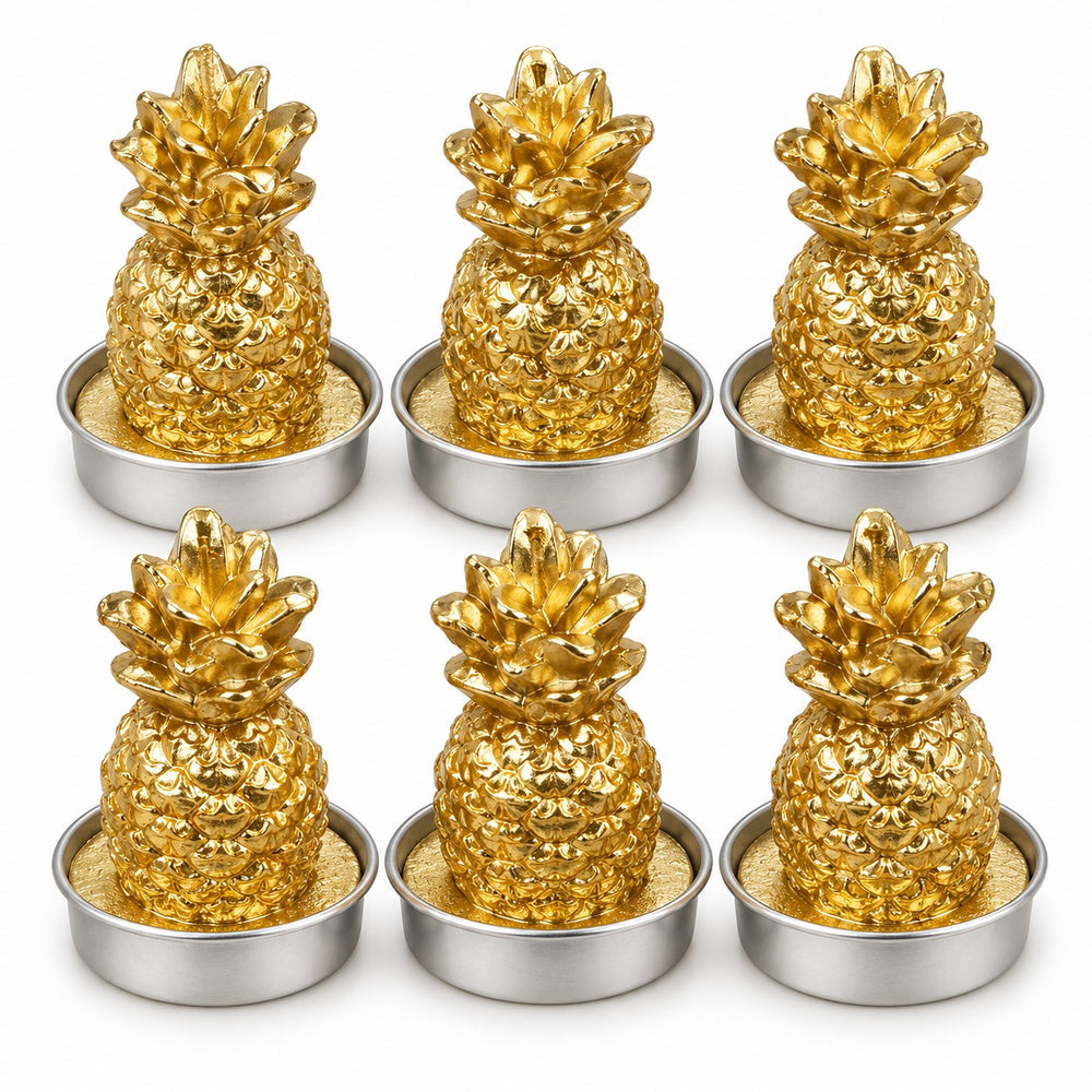 Six gold pineapple-shaped tea light candles with lit flames, arranged in two rows of three on a light marble surface with a warm bokeh background.
