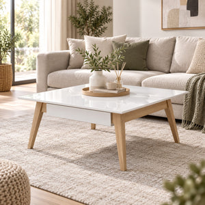 A modern low coffee table with a glossy white rectangular top and light natural wood legs, styled in a bright, contemporary living room with a beige sofa and neutral rug.